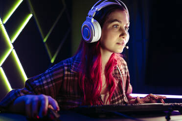 Spielerin, die sich auf ihren Computerbildschirm konzentriert, während sie sich den Herausforderungen eines Online-Videospiels stellt. Weibliche Spielexpertin, die sich der virtuellen Spielwelt stellt und einen Computer und ein Headset zum Spielen benutzt. - JLPSF29893