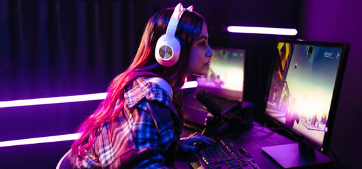 Weibliche Spielerin, die ein Ego-Shooter-Spiel auf einer Online-Plattform spielt. Die Frau sitzt vor einem lebendigen und grafischen Multi-Monitor-Setup, das sich perfekt für Live-Streaming und Immersion von Videospielen eignet. - JLPSF29915