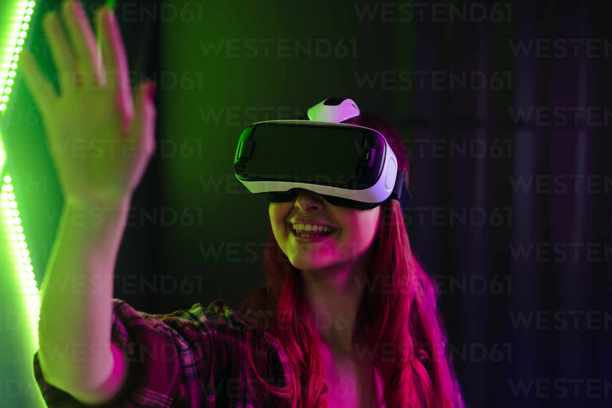 With a VR headset on, a woman reaches out her hand to touch and manipulate  objects in a simulated environment. Female exploring a VR game with  excitement, immersing herself in the metaverse world. stock photo