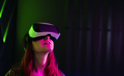 Young woman looking at the immersive digital environment around her with a VR headset. Woman exploring virtual reality and the simulated world created by the futuristic technology. - JLPSF29938