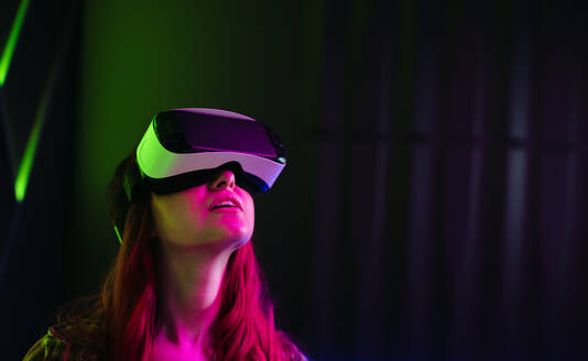 Junge Frau, die mit einem VR-Headset die immersive digitale Umgebung um sich herum betrachtet. Frau, die die virtuelle Realität und die durch die futuristische Technologie geschaffene simulierte Welt erkundet. - JLPSF29938