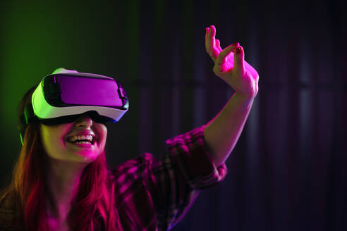 Eine Frau lächelt, während sie sich in die aufregende Welt der virtuellen Realität begibt und die Zukunft des Vergnügens vorstellt. Mit einem VR-Headset auf dem Kopf scheint sie vollständig in die digitale Umgebung einzutauchen. - JLPSF29940
