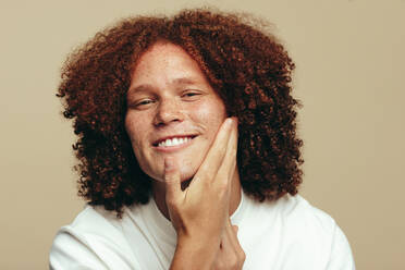 Portrait of a youthful man with ginger hair touching his beautiful, freckled face, feeling proud of his skincare routine. Happy young man maintaining and moisturizing his unique skin. - JLPSF30025