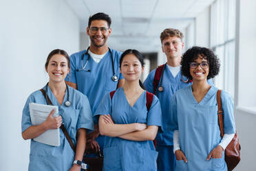 Porträt von erfolgreichen Medizinstudenten, die zusammen in einem Krankenhaus stehen, passende Kittel tragen und fröhlich dreinschauen. Gruppe von verschiedenen Studenten, die gemeinsam ihre medizinische Ausbildung beginnen. - JLPPF01670