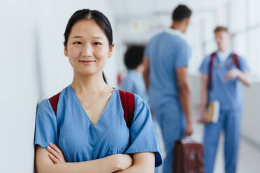 Asiatische Krankenpflegeschülerin, die in einem Krankenhaus in medizinischer Kleidung steht und selbstbewusst in die Kamera blickt. Junge Studentin, die ihre Ausbildung zur Krankenschwester absolviert. - JLPPF01674