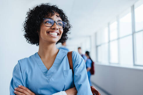 Confident female medical student stands smiling in scrubs, interning at a teaching hospital and learning healthcare and medicine as she prepares for her residency. - JLPPF01677