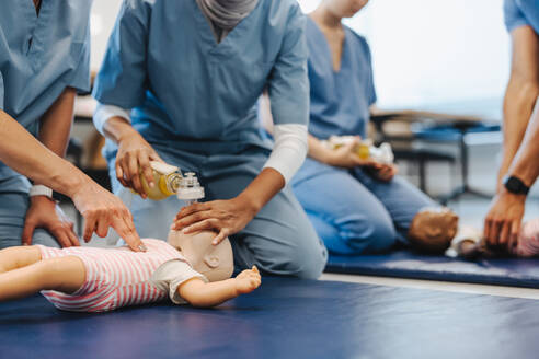 Medizinstudentinnen verwenden bei der Herz-Lungen-Wiederbelebungsschulung eine Beatmungsmaske an einer Babypuppe. Studenten in Kitteln erlernen bei einer medizinischen Simulation die zur Rettung eines pädiatrischen Patienten erforderlichen Fähigkeiten. - JLPPF01714