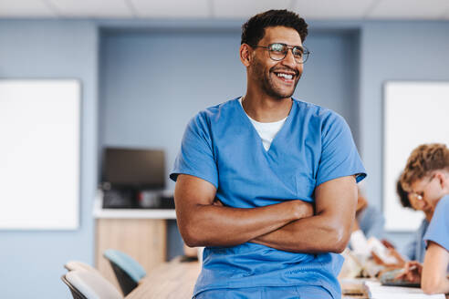 Young medical student sits on a table in a university hospital, smiling and surrounded by health professionals learning and training to become the best healthcare providers. - JLPPF01728