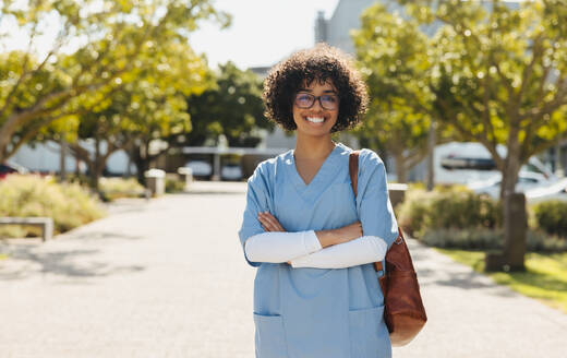 Aspiring doctor, a young woman in medical school, looks at the camera with a confident smile as she stands on campus dressed in scrubs. Smart young woman studying medicine at university. - JLPPF01735