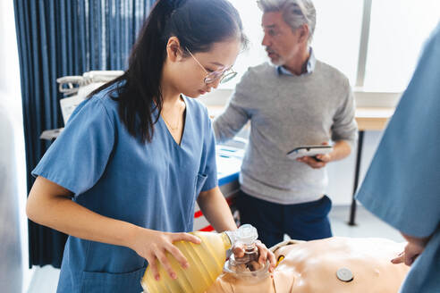 Asiatische Krankenpflegeschülerin, die an einem medizinischen Simulator übt, wie man einem Patienten eine Beatmungsmaske anlegt. Junge Studentin im Kittel, die an einer klinischen Simulationsübung teilnimmt. - JLPPF01745