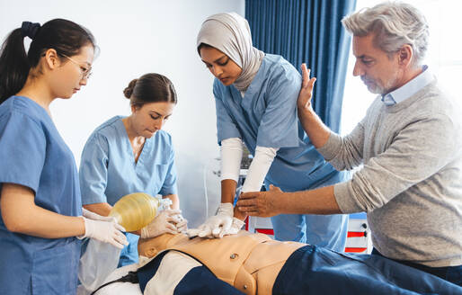 Älteres medizinisches Fachpersonal, das eine Gruppe von Studentinnen in einem medizinischen Simulationstraining anleitet. Ein Arzt unterrichtet Medizinstudenten in der Wiederbelebung mit Herzdruckmassage und Beatmungsmaske. - JLPPF01747