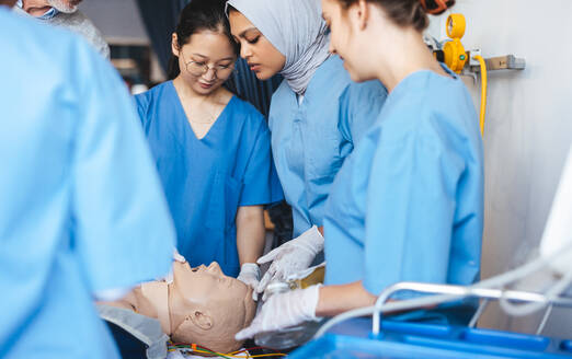 Verschiedene Krankenpflegeschülerinnen, darunter eine, die einen Hidschab trägt, üben während einer medizinischen Simulation Wiederbelebungsmaßnahmen. Weibliche Krankenpflegeschülerinnen in Kitteln nehmen an einer Schulung in der Krankenpflegeschule teil. - JLPPF01750