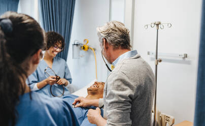 Ein älterer Arzt zeigt seinen Studenten, wie man ein Stethoskop benutzt, um die inneren Körpergeräusche abzuhören. Ein erfahrener Mediziner unterrichtet eine Gruppe junger Studenten in einem Lehrkrankenhaus. - JLPPF01766