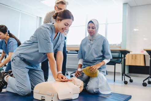 Studentinnen in Kitteln üben unter Aufsicht eines Oberarztes die Herz-Lungen-Wiederbelebung an einer Puppe. Zwei junge Frauen nehmen an einer medizinischen Simulationsübung in einem Lehrkrankenhaus teil. - JLPPF01775