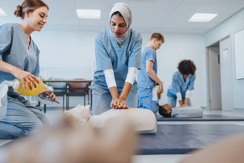 In einem medizinischen Simulationszentrum führen zwei junge Studentinnen in Kitteln im Rahmen ihrer Krankenpflegeausbildung an einer HLW-Puppe Herzdruckmassage und Beatmung mit Beatmungsbeutel durch. - JLPPF01778