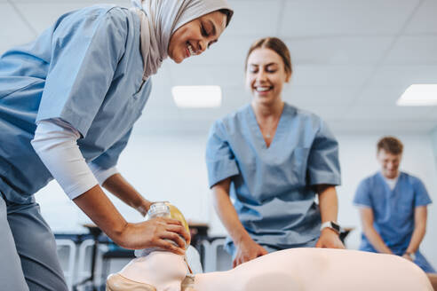 Medizinstudentinnen lächeln fröhlich, während sie mit Puppen und Beatmungsmasken die Herz-Lungen-Wiederbelebung üben. Medizinstudenten verschiedener Fachrichtungen erhalten während ihres klinischen Praktikums eine praktische Lektion über Beatmung. - JLPPF01817