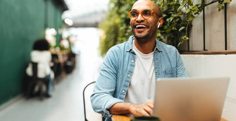 Ein junger Berufstätiger lächelt glücklich, während er mit seinem Laptop aus der Ferne arbeitet. Ein Geschäftsmann erledigt seine Aufgaben in einem Coworking Space, indem er Internetverbindungen und drahtlose Technologie nutzt. - JLPSF30060