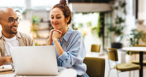 Zwei Kollegen, die Seite an Seite in einem Coworking Space arbeiten und auf einen Laptop-Bildschirm schauen, während sie gemeinsam an einem Projekt arbeiten. Junge Geschäftsleute, die mit ihrer Zusammenarbeit zufrieden sind. - JLPSF30063