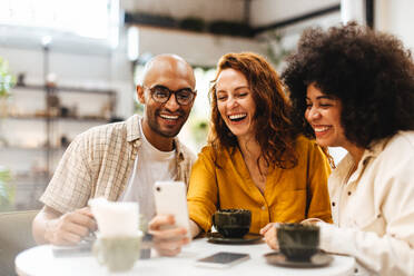 Freunde führen in einem Café einen Videoanruf durch und unterhalten sich mit anderen Freunden, während sie in einem Restaurant einen Kaffee trinken. Eine Gruppe junger Leute hängt fröhlich zusammen ab. - JLPSF30082