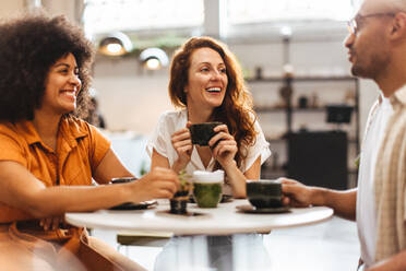 Group of friends catch up over coffee in a cozy cafe, taking a break from their busy lives to spend time together and reconnect. Happy young people gathering in a relaxed and social environment. - JLPSF30090