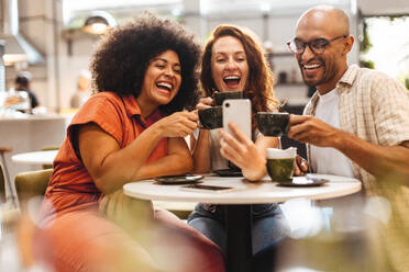 Drei Freunde machen ein Selfie in einem gemütlichen Café, umgeben vom Duft des frisch gebrühten Kaffees - JLPSF30092