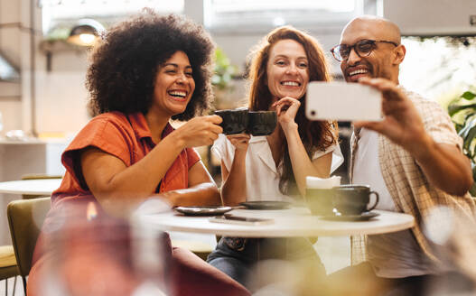 Drei Freunde genießen Kaffee und die Gesellschaft des anderen und halten den Moment mit albernen Selfies in einem gemütlichen Café fest - JLPSF30093