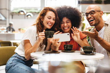 Fröhliche junge Leute, die mit ihren Freunden über ein Mobiltelefon einen lustigen Videochat führen. Eine Gruppe fröhlicher und unterschiedlicher Freunde, die in ihrem Lieblingscafé zusammen abhängen. - JLPSF30098