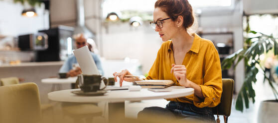 Postgraduate student works diligently on her studies at a cozy cafe. Woman using a laptop to do her research with online scholarly articles, determined to succeed in her academic pursuits. - JLPSF30112