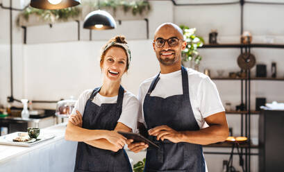 Zwei Unternehmer im Gastgewerbe, die selbstbewusst in ihrem kleinen Café stehen. Ein erfolgreicher Mann und eine erfolgreiche Frau, die als Team arbeiten, um das Tagesgeschäft zu bewältigen und ihren Kunden einen hervorragenden Service zu bieten. - JLPSF30133