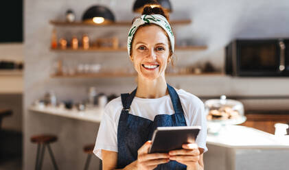 Selbstbewusste Café-Besitzerin, die ihr kleines Unternehmen mit einem Tablet verwaltet. Die Frau nutzt Technologie, um ihren Kunden einen effizienten Service zu bieten und den Erfolg ihres Cafés zu sichern. - JLPSF30136