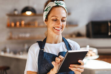 Zufriedene Frau, die ein Touchscreen-Tablet verwendet, um ihr Café effizient zu verwalten. Die Unternehmerin konzentriert sich auf die Aufrechterhaltung eines reibungslosen Betriebs und die Bereitstellung eines hochwertigen Kundendienstes. - JLPSF30137