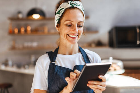 Zufriedene Frau, die ein Touchscreen-Tablet verwendet, um ihr Café effizient zu verwalten. Die Unternehmerin konzentriert sich auf die Aufrechterhaltung eines reibungslosen Betriebs und die Bereitstellung eines hochwertigen Kundendienstes. - JLPSF30137