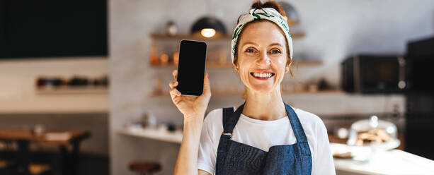 Frau, die den Einsatz von Smartphones für das Restaurantmanagement befürwortet. Glückliche Unternehmerin, die moderne technische Hilfsmittel empfiehlt, um den Erfolg von Kleinunternehmen im Gastgewerbe zu gewährleisten. - JLPSF30138
