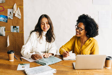 Young business women, a fashion designer and her colleague discuss creative fabric designs in a meeting. Female fashion designers using technology to work together for their small business startup. - JLPSF30148