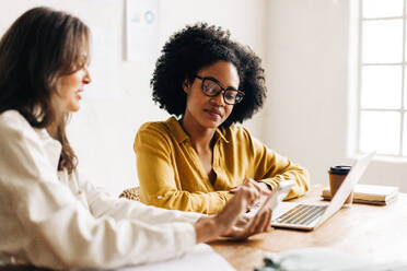 Geschäftsfrauen, die gemeinsam ein Smartphone benutzen und über Ideen und Lösungen für ihr Start-up diskutieren. Zwei kreative Modedesigner - JLPSF30154