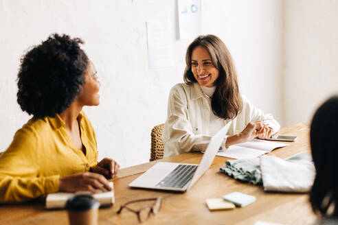 Ein weibliches Team von Geschäftsleuten, darunter eine Modedesignerin und eine Unternehmerin, arbeitet glücklich in einem Büro zusammen, um den Erfolg ihres kleinen Unternehmens zu planen. - JLPSF30155