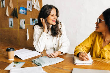 Diverse business women collaborating in a fashion design office, planning a project together. Two young clothing designers smiling confidently as they build a successful small business. - JLPSF30158