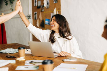 Happy fashion designers giving each other a high five, celebrating their successful collaboration and teamwork. Business women beaming with joy and excitement as they work together on new designs. - JLPSF30162