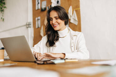 Professional business woman working on her laptop at a table in a design office. Creative woman working on fashion designs for her small business. - JLPSF30168