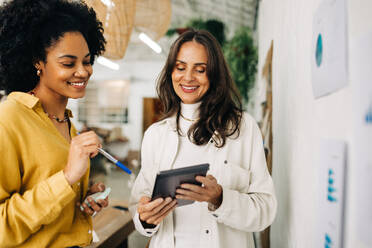 Glückliche Unternehmerinnen, die mit einem Tablet Ideen für ihr Unternehmen sammeln. Zwei Geschäftsfrauen, die als Team arbeiten, um Erfolg und Gewinn in ihrem Start-up zu erzielen. - JLPSF30183