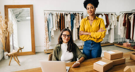 Female entrepreneurs looking at the camera, confident in their abilities as small business owners who run an online clothing store. Two business women working together to grow their ecommerce startup. - JLPSF30201