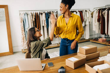 Zwei junge Frauen, die gemeinsam einen Online-Shop betreiben, der Dropshipping-Dienste anbietet, geben sich gegenseitig ein High Five und feiern ihren Erfolg im E-Commerce. - JLPSF30203