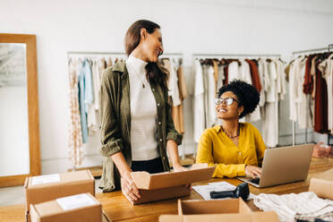 Erfolgreiche Geschäftsfrauen, die mit einem Online-Kleiderladen Bestellungen für das Dropshipping abwickeln. Zwei glückliche Unternehmerinnen, die ihr Einzelhandelsgeschäft mit einer E-Commerce-Website erweitern. - JLPSF30206