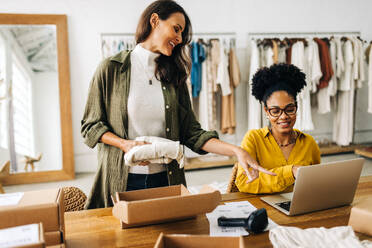 Frauen arbeiten zusammen, um die Bestellungen für ihre E-Commerce-Website in einer Bekleidungsboutique auszuführen. Zwei Unternehmerinnen, die als Team ein erfolgreiches Dropshipping-Geschäft betreiben. - JLPSF30209