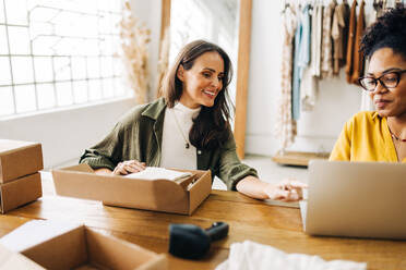 Boutique-Besitzerinnen, die einen Online-Shop für ihr Einzelhandelsgeschäft einrichten. Zwei glückliche Geschäftsfrauen, die ihre ersten Dropshipping-Bestellungen abwickeln, während sie ihr Start-up mit einer E-Commerce-Website erweitern. - JLPSF30211