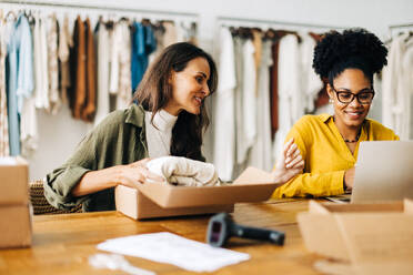 Geschäftsfrauen, die in einer Bekleidungsboutique eine E-Commerce-Website einrichten und ihre ersten Bestellungen für den Direktversand abwickeln. Zwei Frauen, die ihr Unternehmertum mit einem Online-Shop erweitern. - JLPSF30213