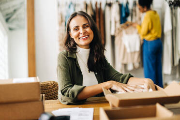 Erfolgreiche Unternehmerin lächelt, während sie in einer Bekleidungsboutique Bestellungen für ihr Dropshipping-Geschäft ausführt. Glückliche Geschäftsfrau, die ihr kleines Unternehmen mit einem Online-Shop erweitert. - JLPSF30214