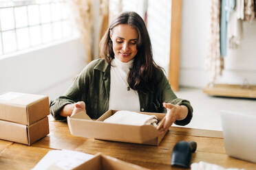 Female online store owner doing order fulfilment in her boutique, packaging clothing products into biodegradable boxes. Woman using dropshipping to run her small business. - JLPSF30217
