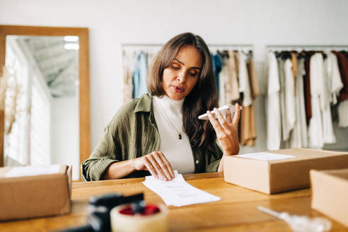 Ecommerce business owner gets on the phone to discuss barcode labels as she processes clothing orders. Woman communicates with her shipping partners, planning smooth and swift delivery of packages. - JLPSF30234