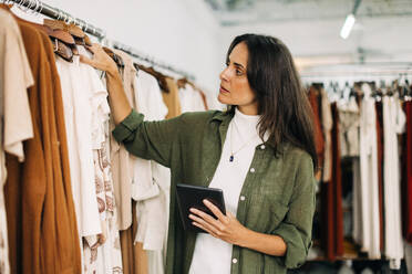 Clothing store owner conducting a stock take in her shop with the help of a trusty tablet. Focused business woman checking and counting items to ensure her inventory is accurate and up-to-date - JLPSF30248